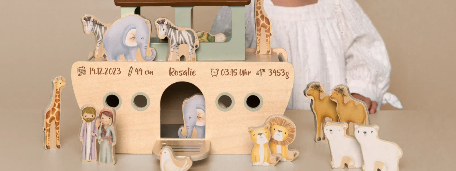 Personalisierte Holz-Arche Noah zur Taufe mit graviertem Namen, Geburtsdatum, Uhrzeit und Gewicht, dekoriert mit Holzfiguren von Tieren und Menschen vor neutralem Hintergrund.