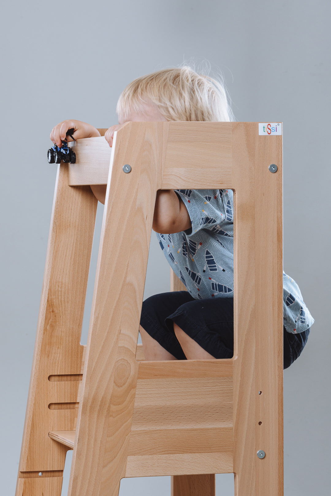 Child playing with a natural wood learning tower by tiSsi® by Schmatzepuffer® in a neutral background