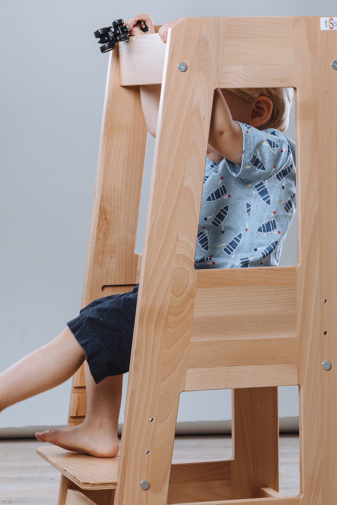 Child sitting in natural wood Lernturm Felix learning tower by tiSsi, playing with toy binoculars indoors