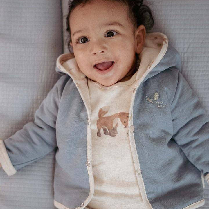 Baby trägt eine weiche Wendejacke in Stone Blue und lächelt – hochwertige Babykleidung für Neugeborene, ideal als Geschenk zur Geburt