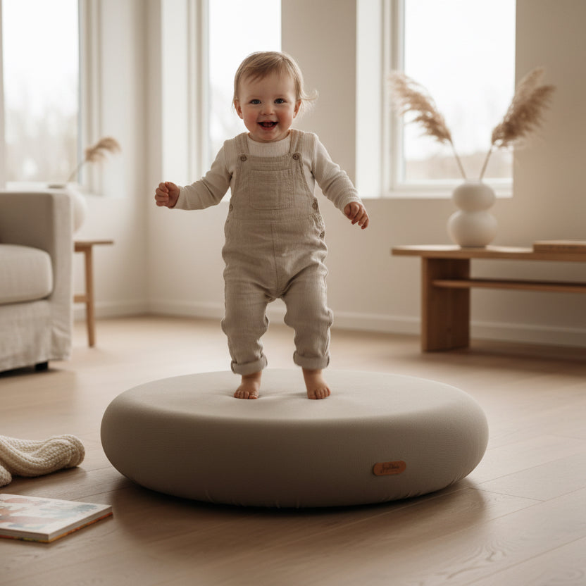 Kleinkind hüpft auf Indoor Sprungkissen in dunklem Beige in hellem Wohnzimmer, sicheres Spielzeug für Bewegung und Gleichgewicht
