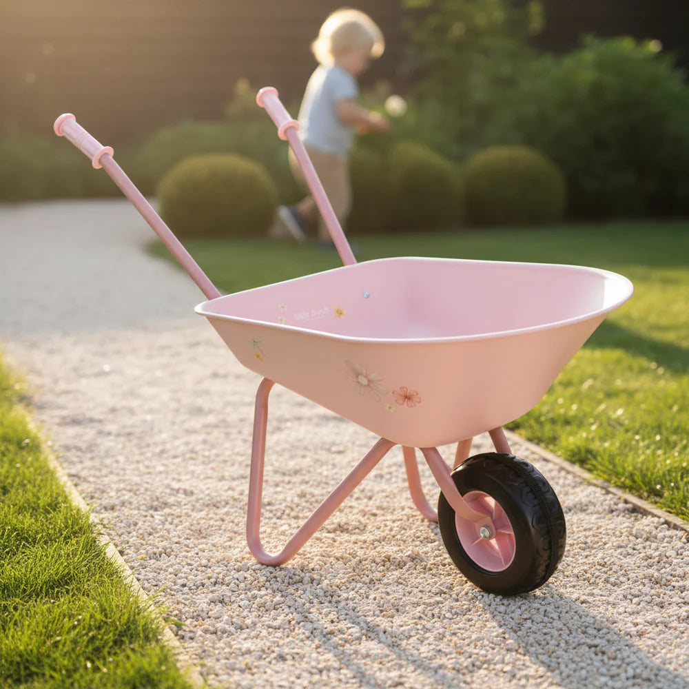 Rosa Kinder-Schubkarre aus Metall auf einem hellen Gartenweg im warmen Abendlicht